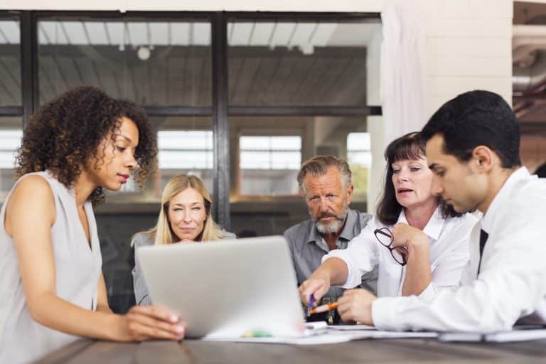 A group of people sitting around a table looking at a laptop.
