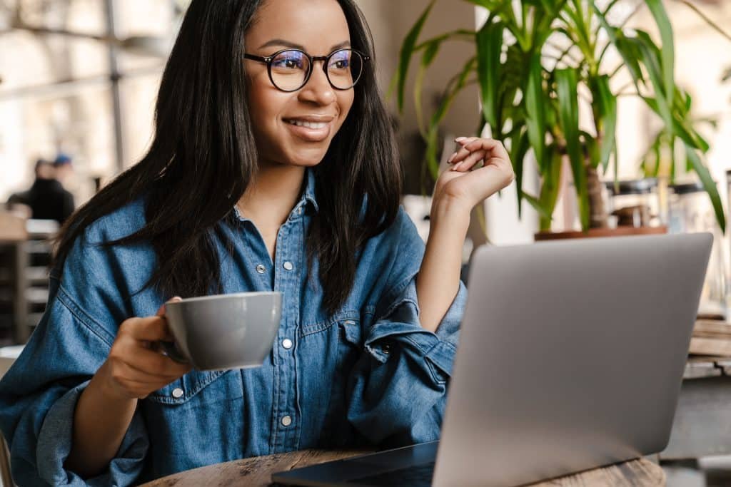 A woman with glasses and a cup of coffee sitting at a table with a laptop.