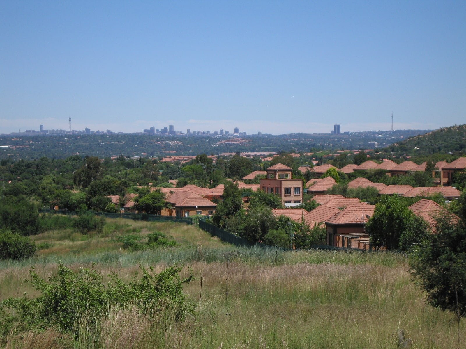 A daytime view of a suburban area with clusters of homes in the foreground and a city skyline in the distance against a clear sky.