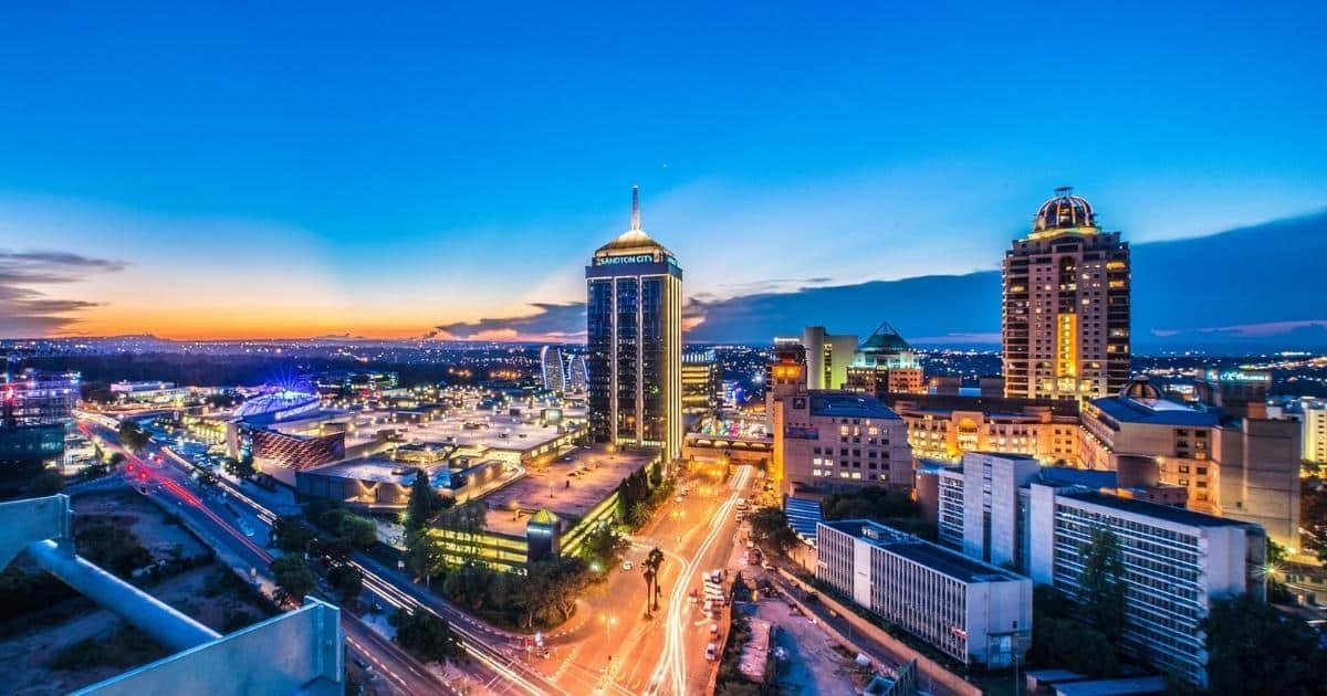 Twilight over a bustling cityscape with illuminated streets and high-rise buildings against a gradient sunset sky.