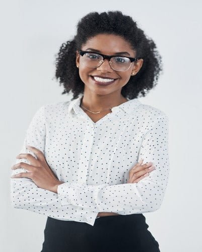 A woman wearing glasses and a polka-dot blouse stands with her arms crossed, smiling.
